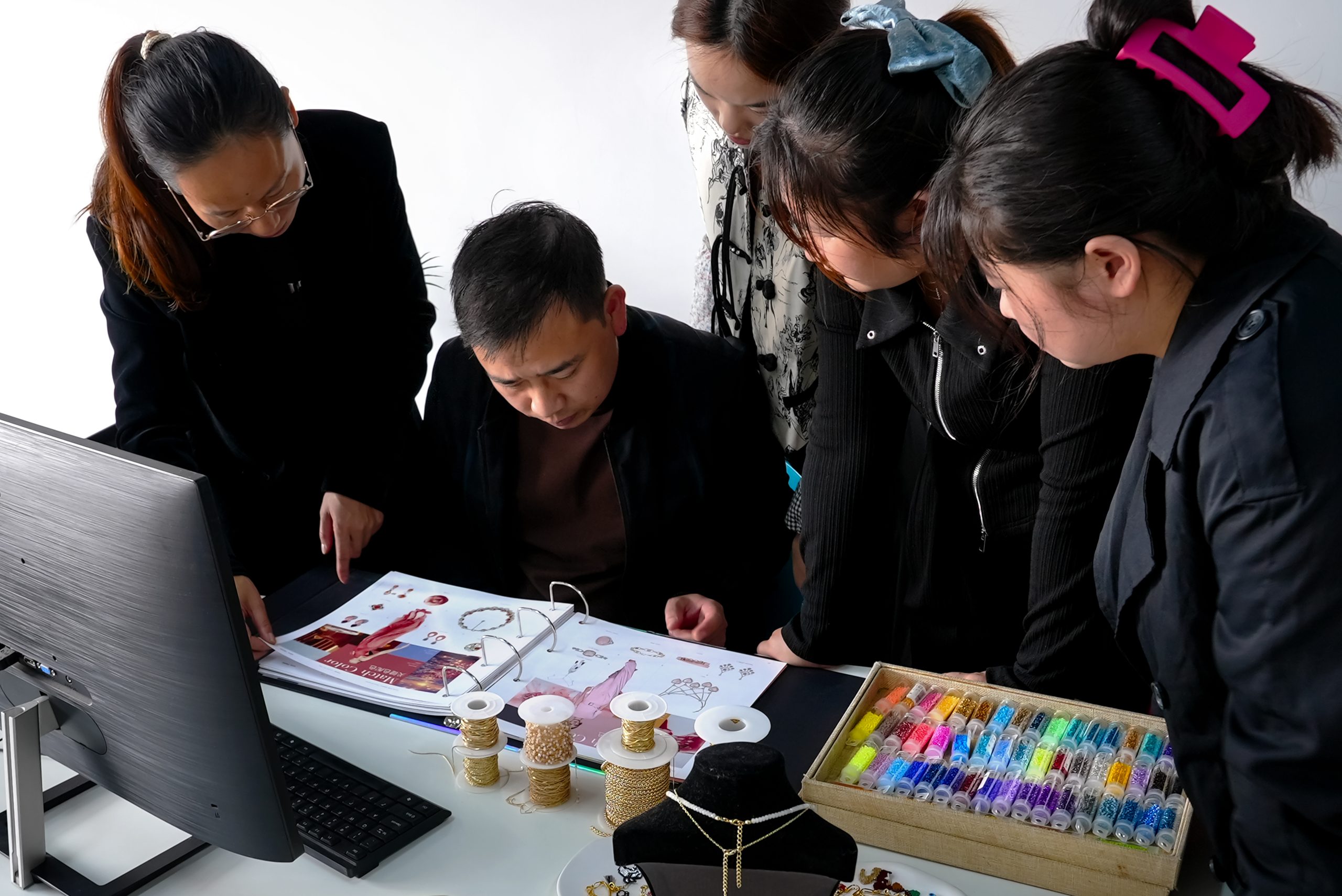 A team of professionals is gathered around a desk, discussing jewelry designs and production details